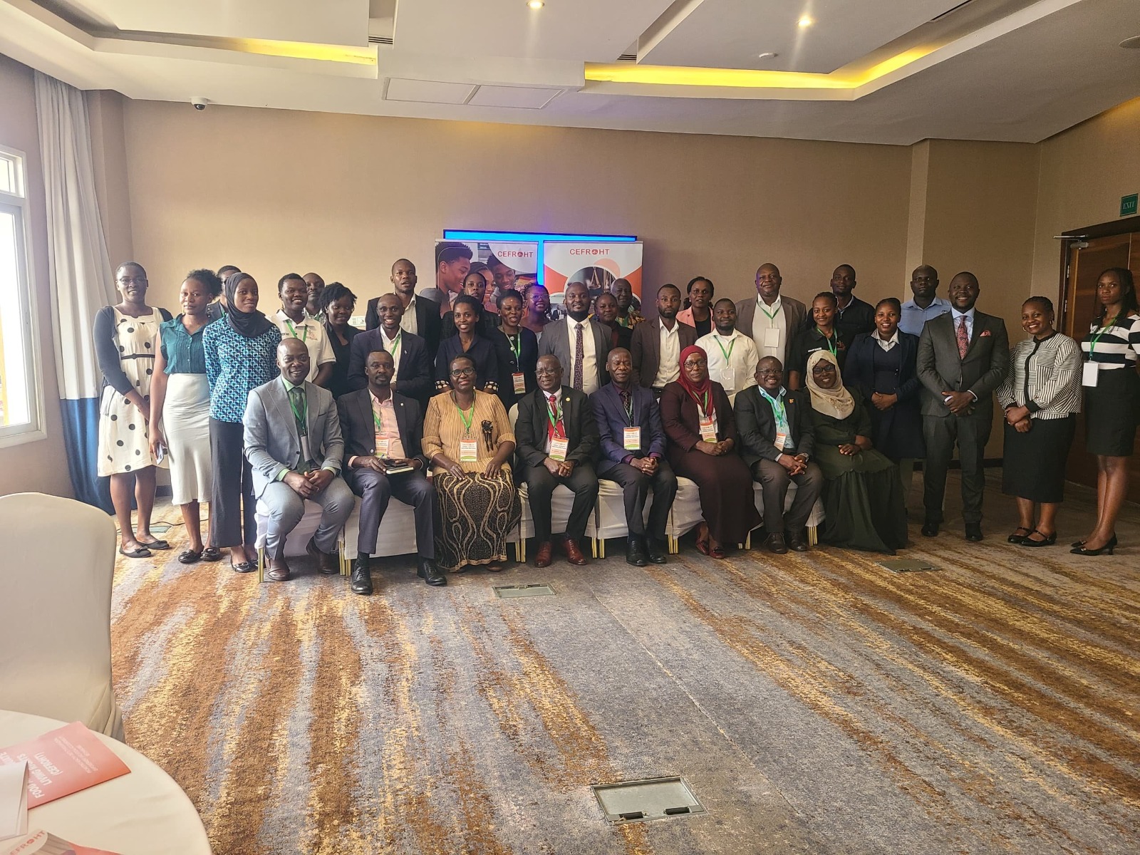 Group photograph of coalition partners seated and standing together in a conference room, many wearing event lanyards.